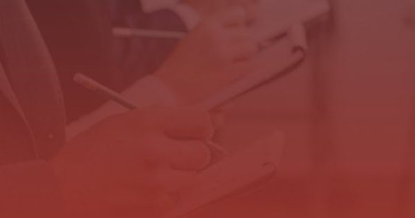 Several people in business attire write on notepads while standing in a line, with a blurred car visible in the background.