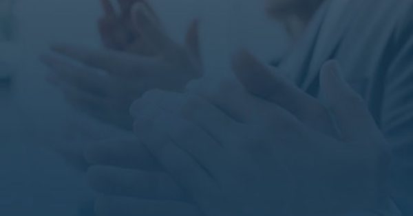 People sitting and applauding, with their hands in focus and faces partially visible, in what appears to be a formal or professional setting.